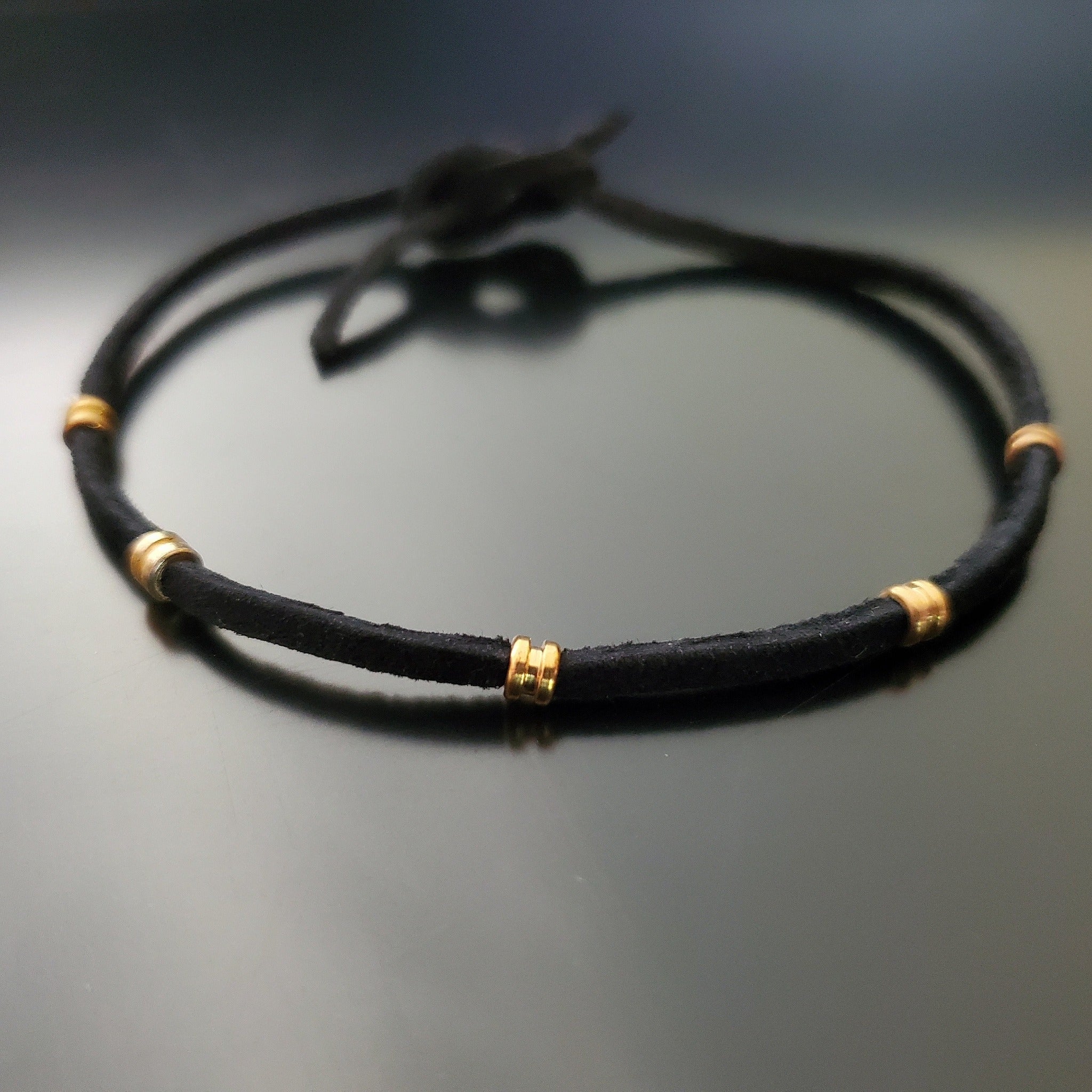 black bracelet made from a suede cord and gold coloured guitar string ballends