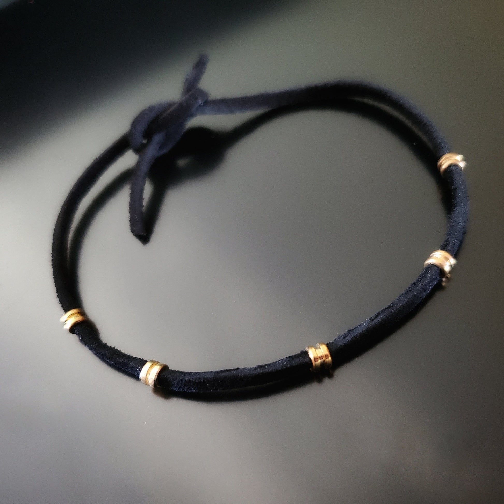 black bracelet made from a suede cord and gold coloured guitar string ballends