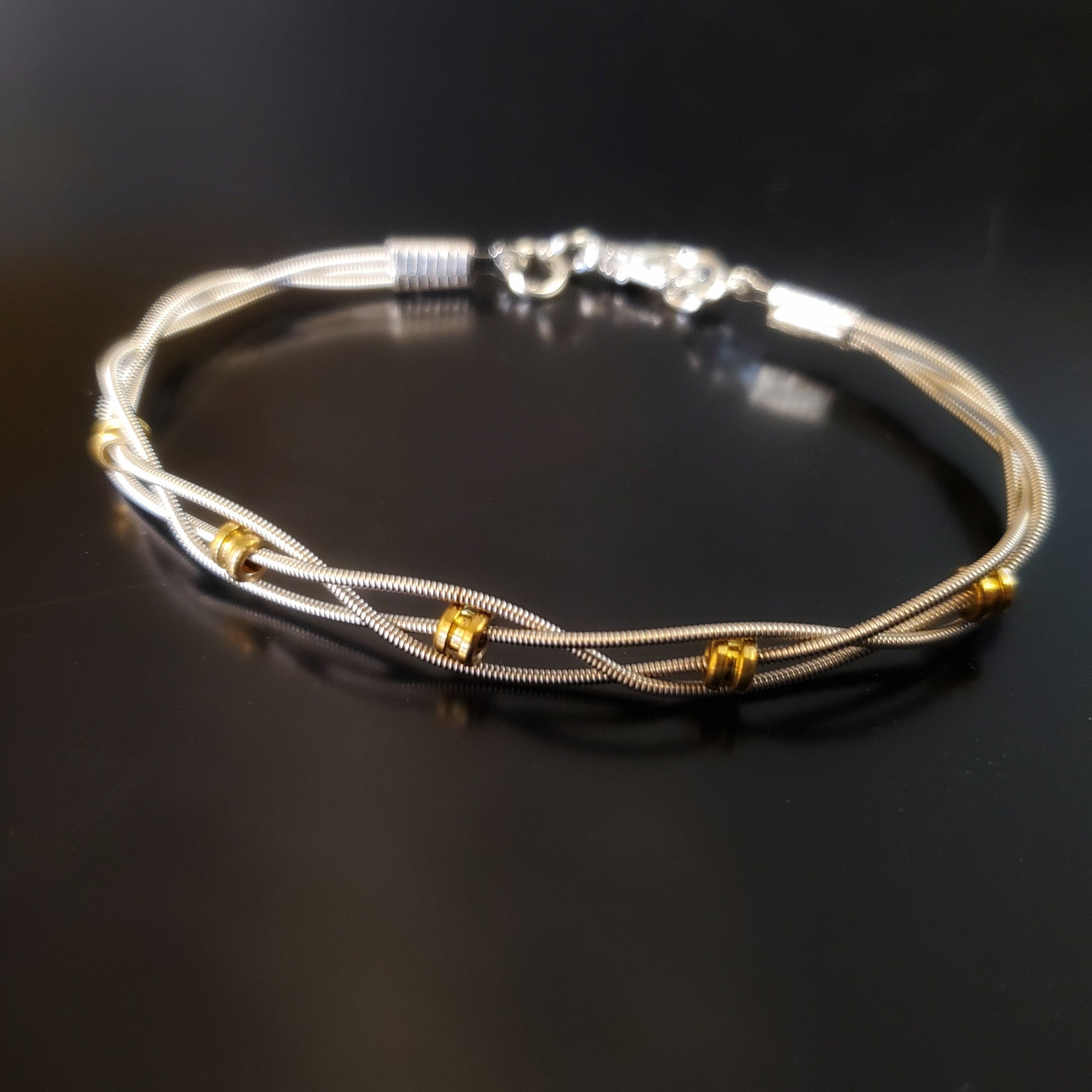 bracelet made with 3 strands of silver coloured guitar strings and 5 gold coloured guitar string ballends on a black background