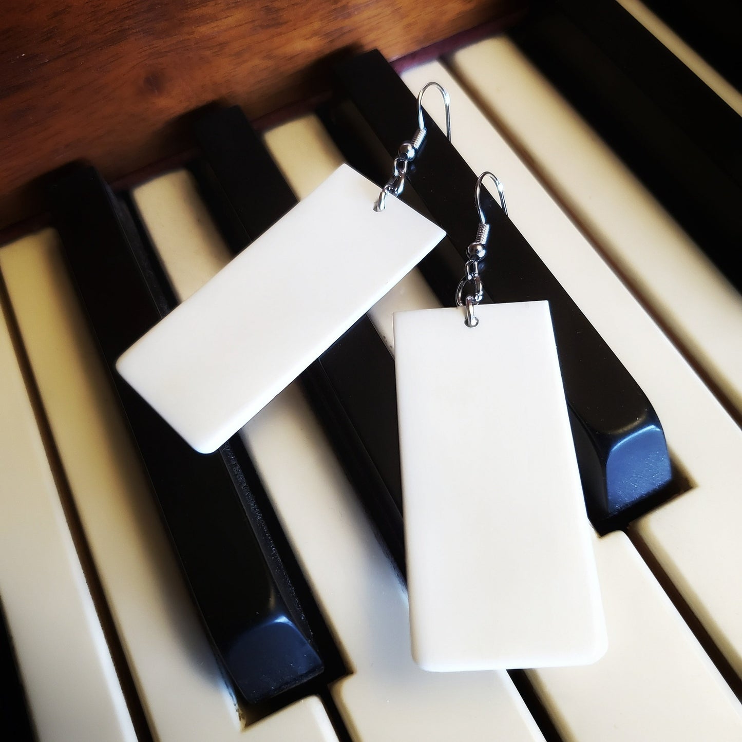 a pair of earrings made from upcycled ivory piano key toppers - the earrings sit on piano keys