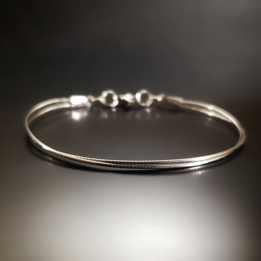 silver coloured bracelet made from an upcycled cello string - black and grey background