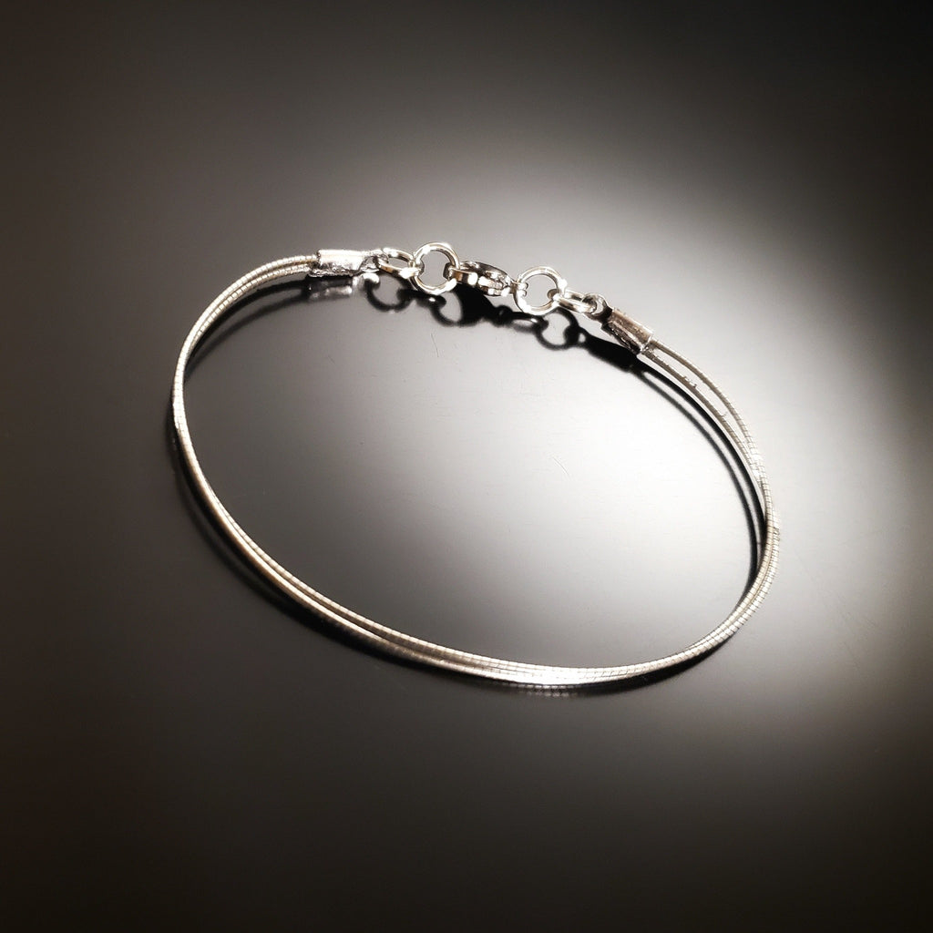 silver coloured bracelet made from an upcycled cello string - black and grey background