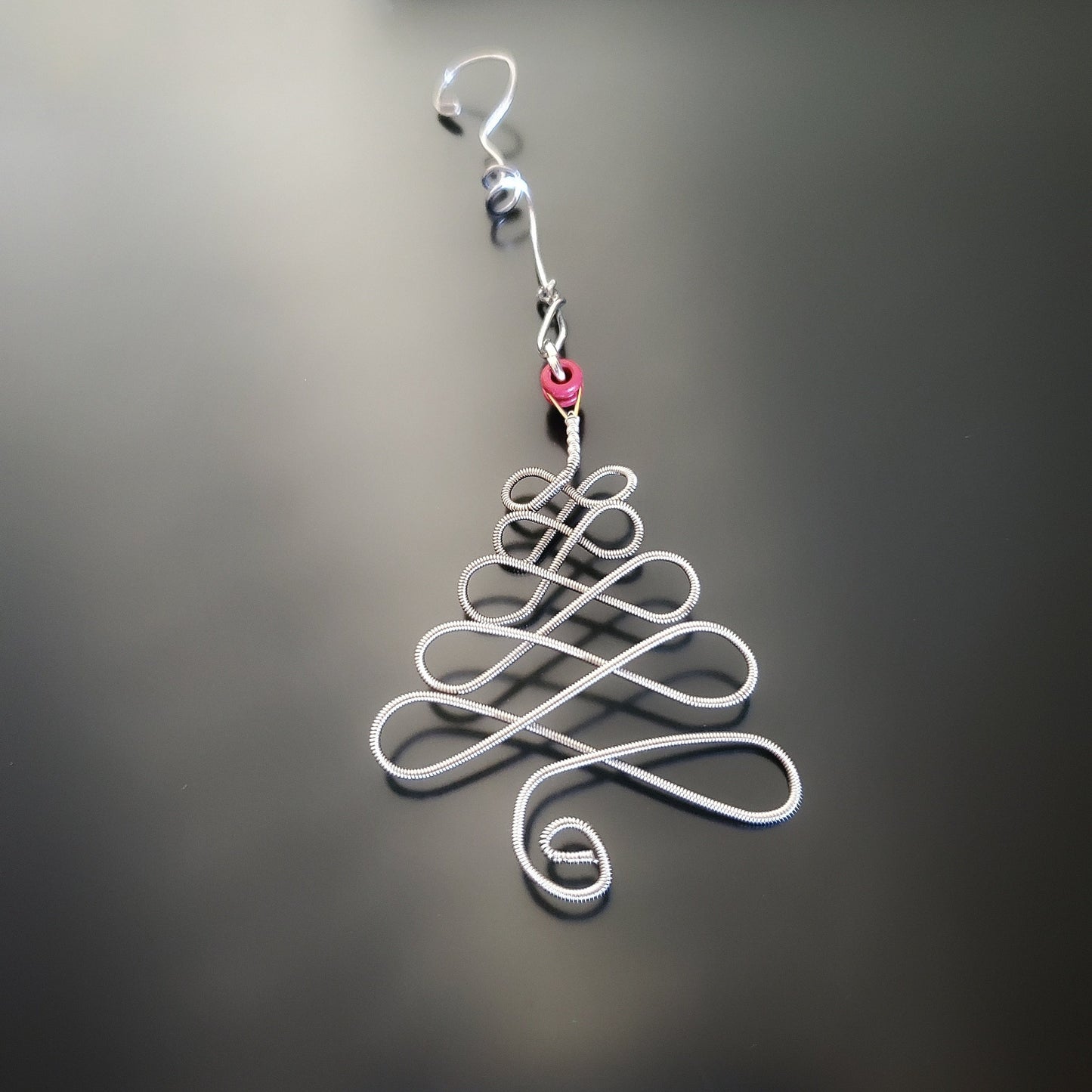 a silver coloured christmas decoration in the shape of a christmas tree made from an upcycled guitar string next to a light blue guitar pick on which there is a white circle and a picture of a black guitar - black and grey background
