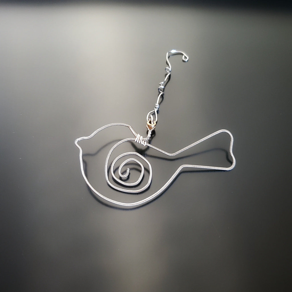 bird shaped christmas decoration made from a hammered guitar string on a black background
