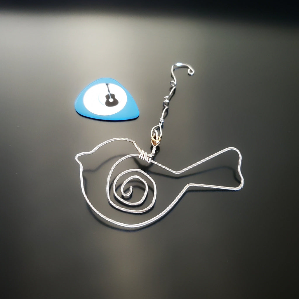 bird shaped christmas decoration made from a hammered guitar string. Blue guitar pick with a picture of a guitar on it. Both on a black background