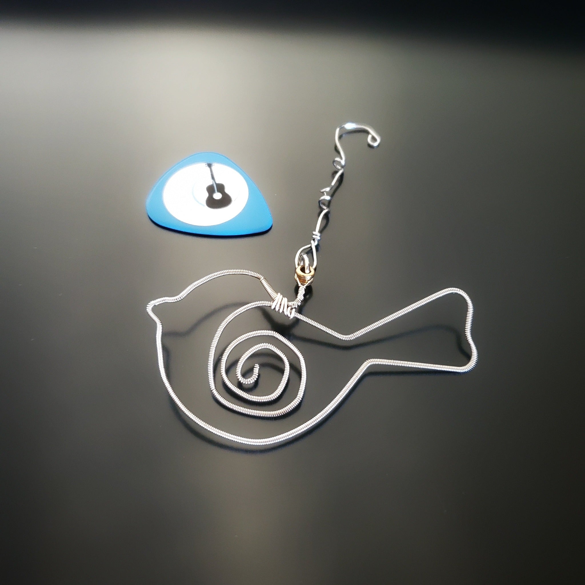 bird shaped christmas decoration made from a hammered guitar string. Blue guitar pick with a picture of a guitar on it. Both on a black background
