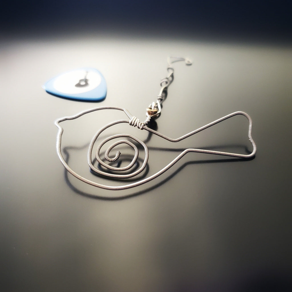 bird shaped christmas decoration made from a hammered guitar string. Blue guitar pick with a picture of a guitar on it. Both on a black background