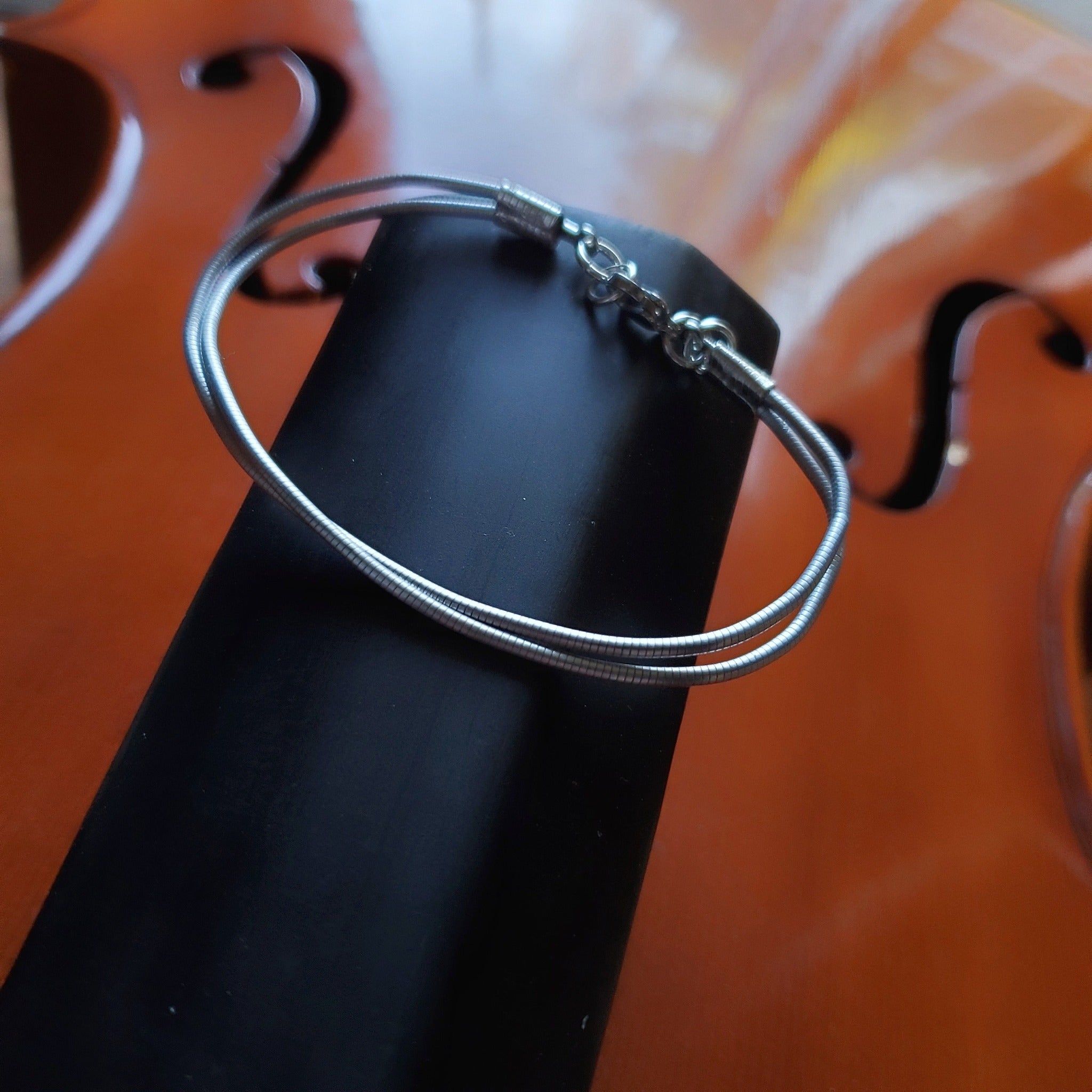 silver coloured bracelet made from an upcycled cello string - the bracelet is sitting on the neck of a cello which doesn't have any strings