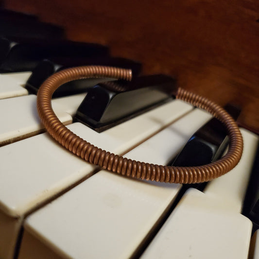 copper cuff style bracelet made from an upcycled piano string - bracelet is lying on piano keys