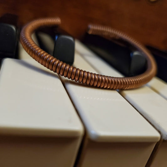 copper cuff style bracelet made from an upcycled piano string - bracelet is lying on piano keys