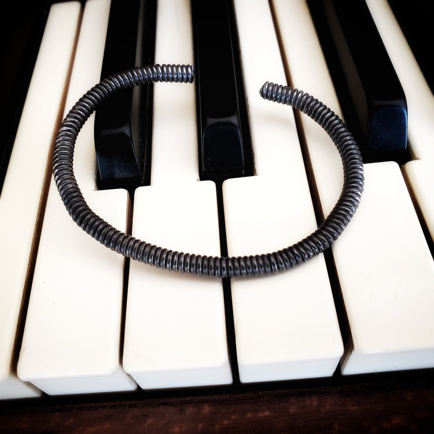 charcoal grey cuff style bracelet made from an upcycled piano string - bracelet is lying on piano keys