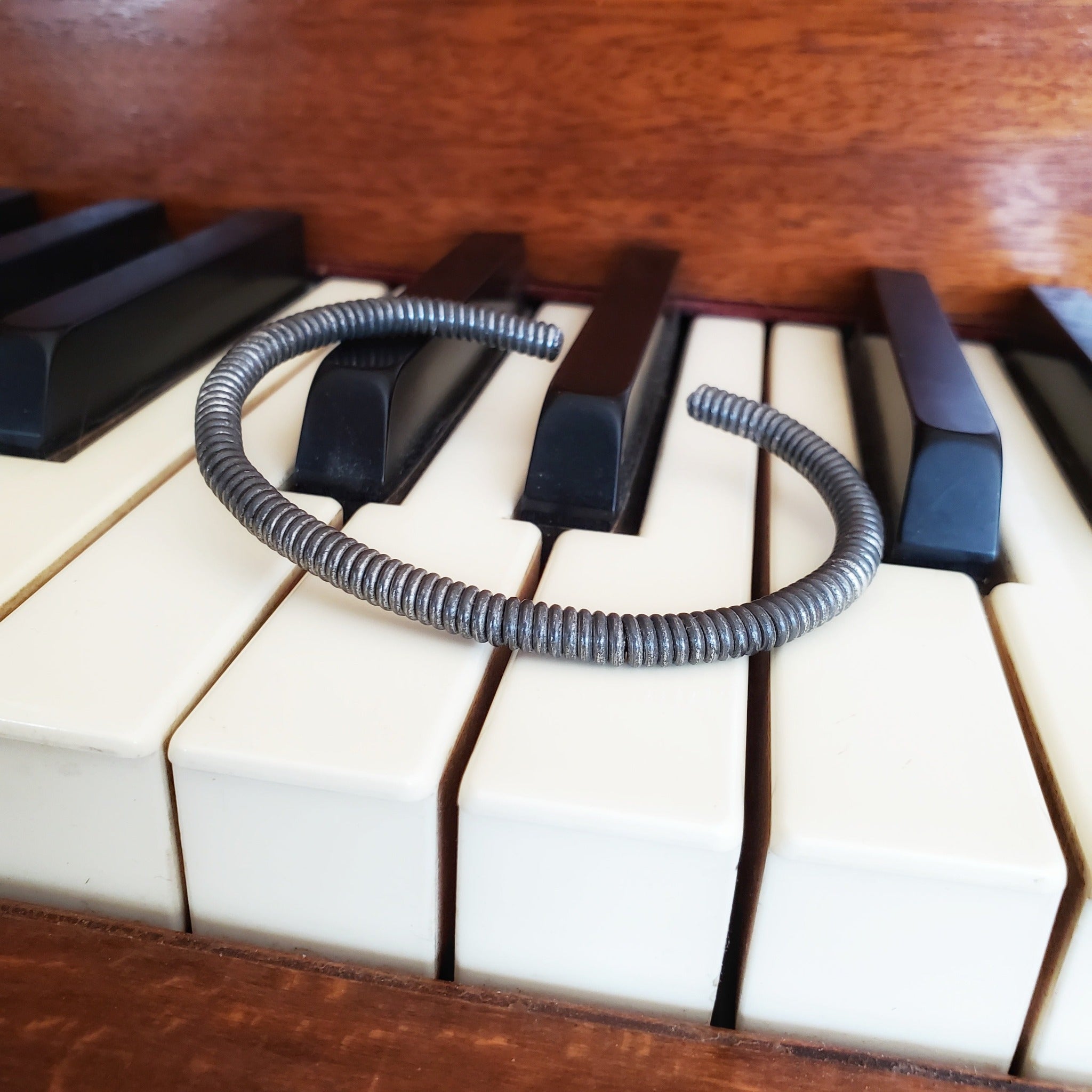 charcoal grey cuff style bracelet made from an upcycled piano string - bracelet is lying on piano keys