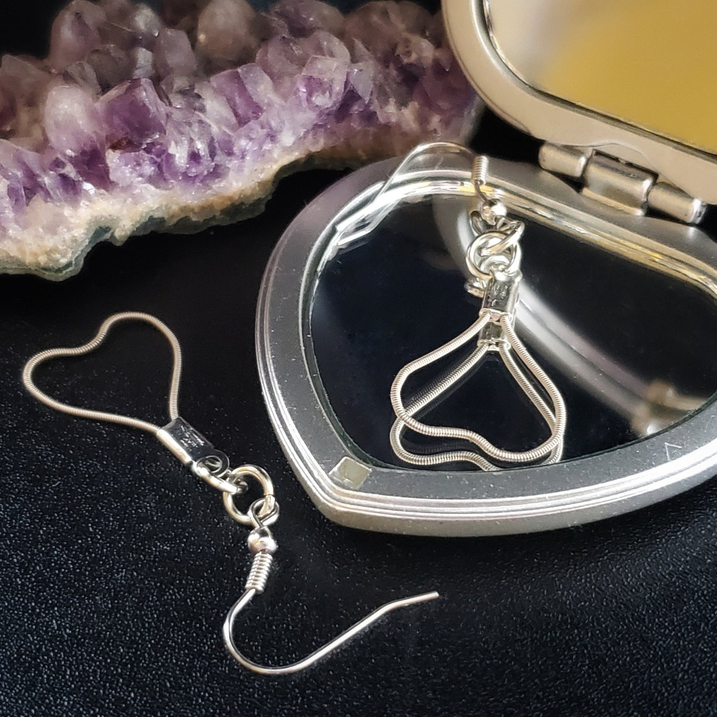 pair of heart shaped earrings made from upcycled guitar strings on a silver coloured heart shaped mirror next to a piece of amethyst