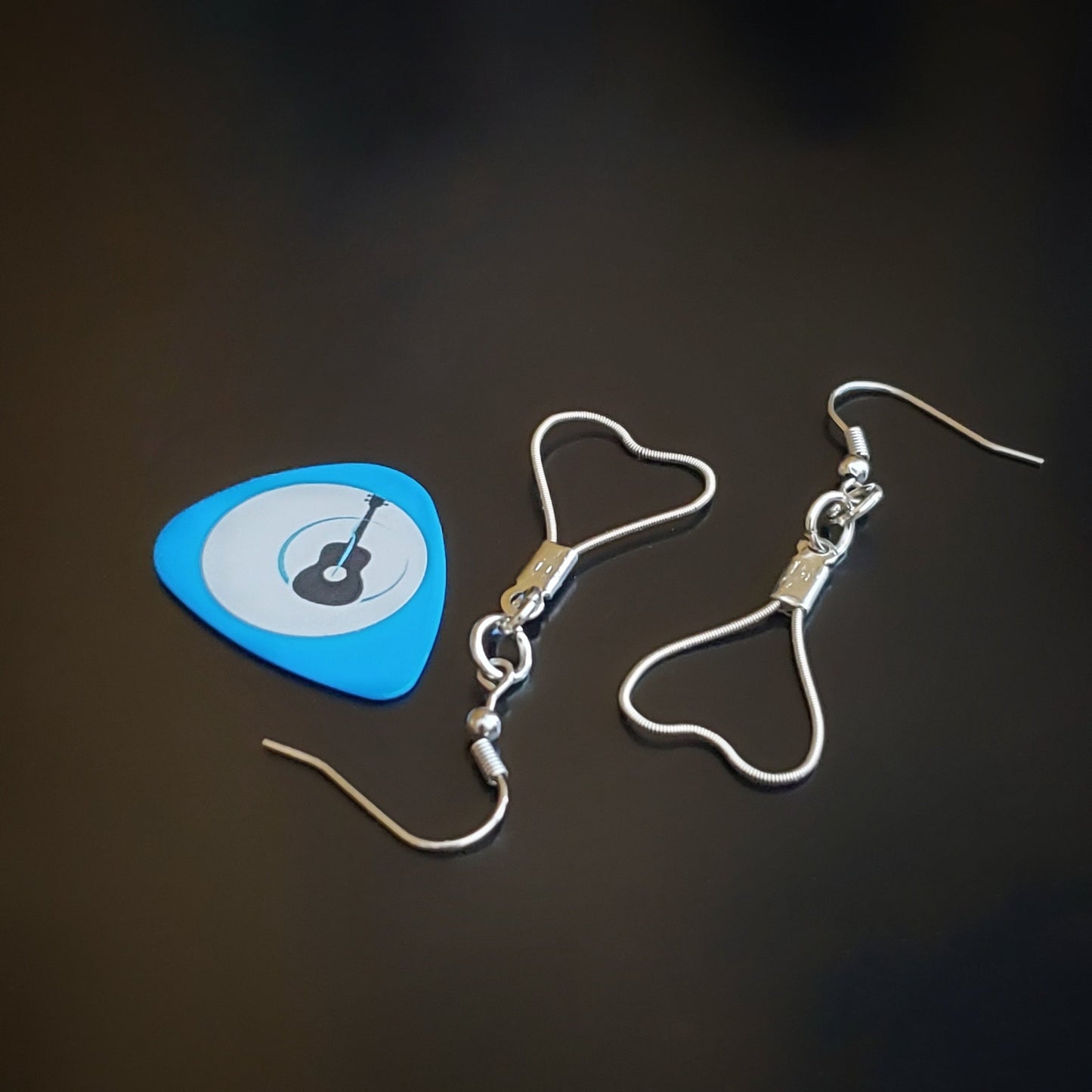 pair of heart shaped earrings made from upcycled guitar strings next to a blue guitar pick with the image of a black guitar