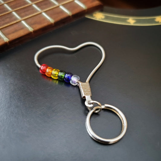 keychain made from an upcycled guitar string - 6 glass beads represent the colours of the LGBTQ flag (red, orange, yellow, green, blue and purple) - on a black guitar body