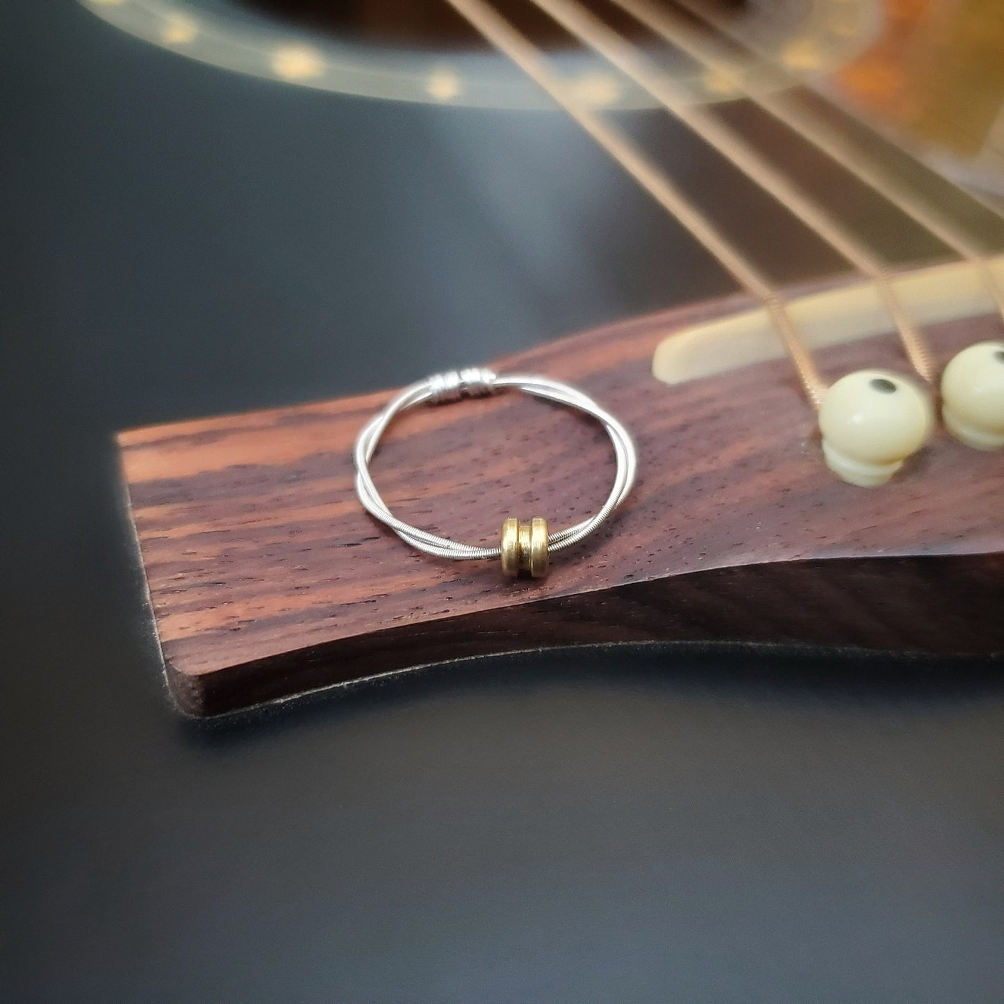 guitar string fidget ring with a gold coloured ballend sitting on the bridge of a black guitar