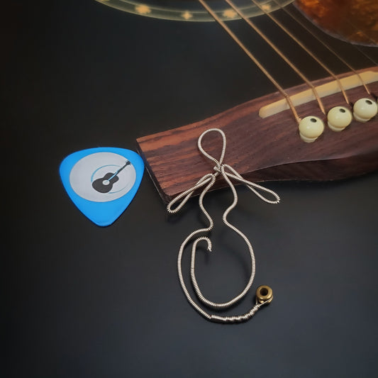 bookmark in the shape of a woman's form - made from an upcycled guitar string- on the left is a blue guitar pick with an image of a black guitar - the bookmark is lying on the bridge of a black guitar