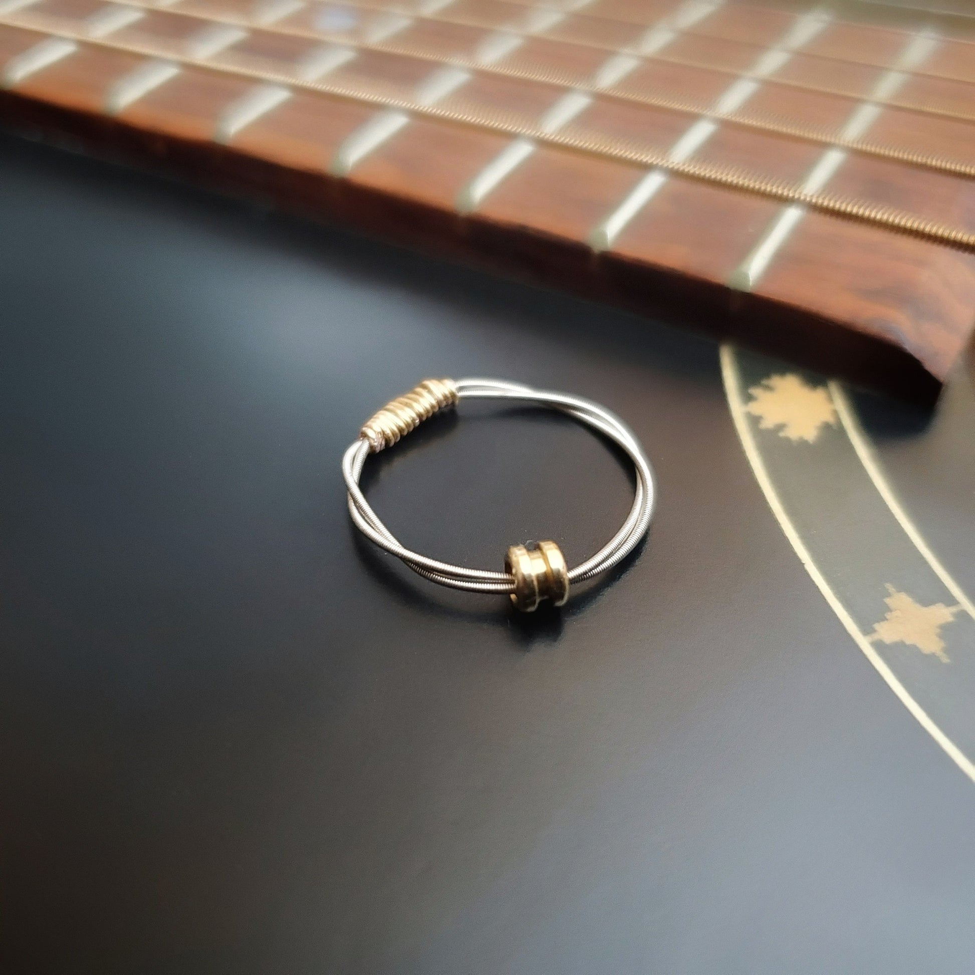 guitar string fidget ring with a gold coloured ballend sitting on a black guitar