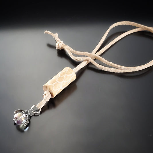 necklace made from a piece of upcycled drumstick on which dragon scales are etched under the drumstick a silver coloured dragon claw pendant holds a clear bead - a beige swede cord holds the pendant - black background