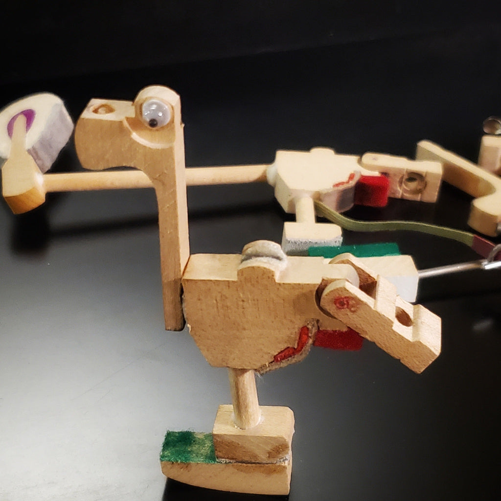 a magnet in the shape of a dinosaur-like animal made from pieces of a piano mechanism - behind it are pieces of piano mechanism like those from which it was made