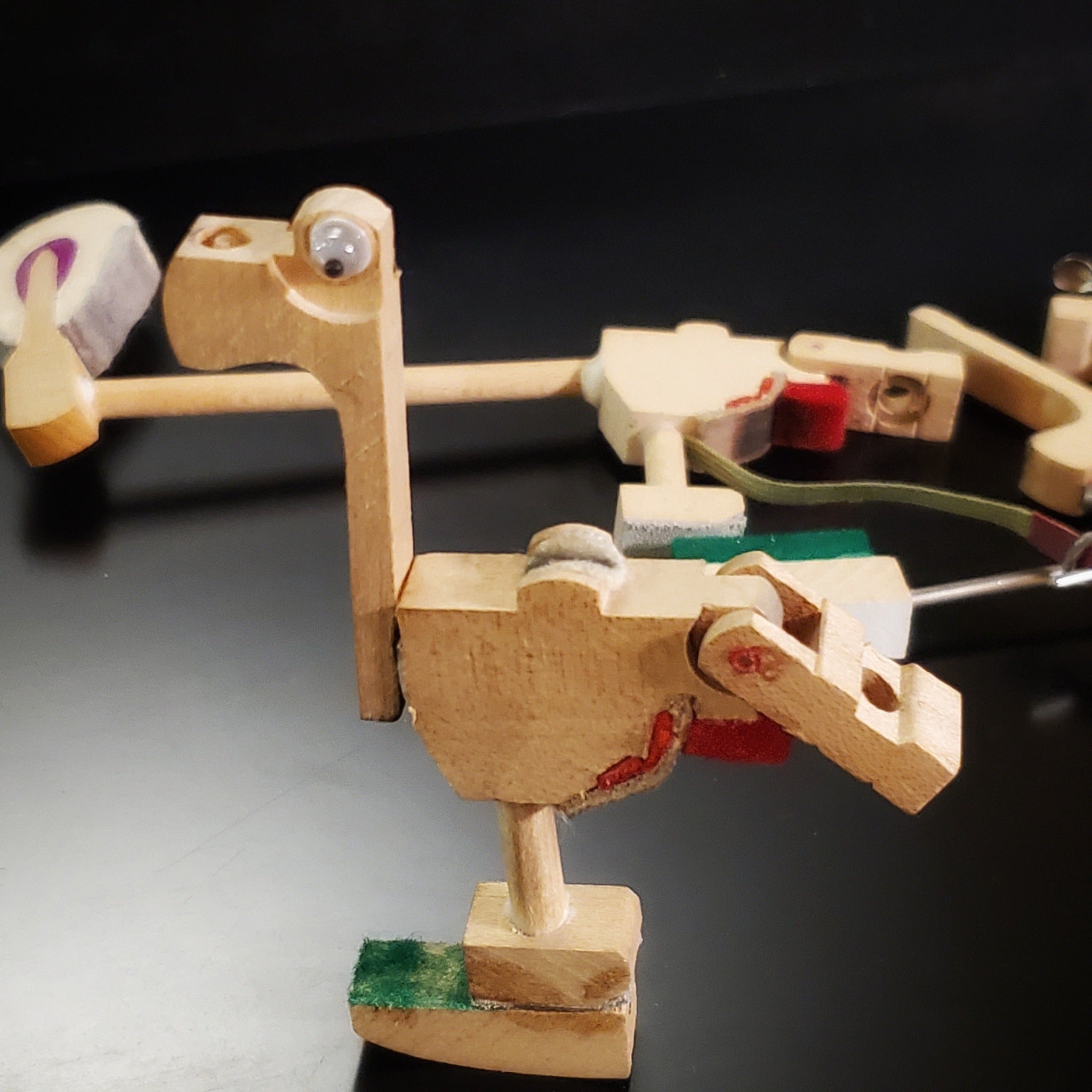 a magnet in the shape of a dinosaur-like animal made from pieces of a piano mechanism - behind it are pieces of piano mechanism like those from which it was made