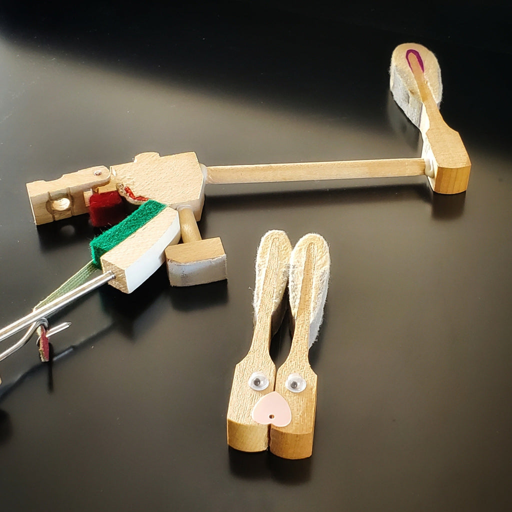 magnet in the shape of a bunny's head - made from 2 upcycled piano hammers - beside it are pieces of a piano's mechanism