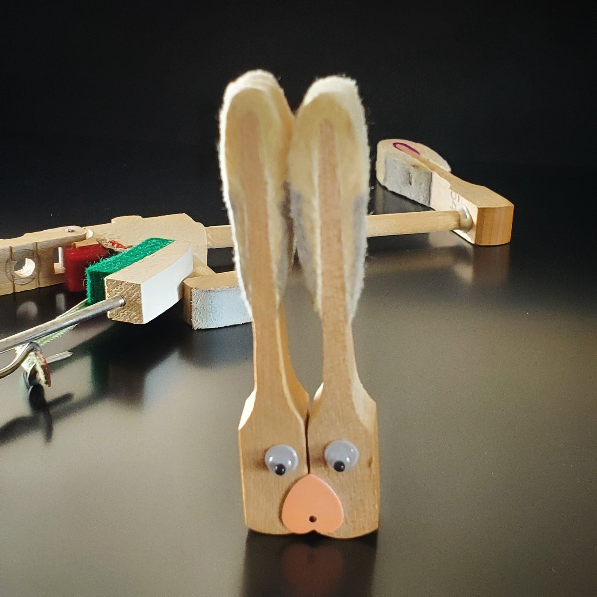 magnet in the shape of a bunny's head - made from 2 upcycled piano hammers - several pieces of a piano's mechanism are in the background