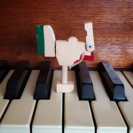 a magnet in the shape of a chicken made from pieces of a piano mechanism standing on piano keys