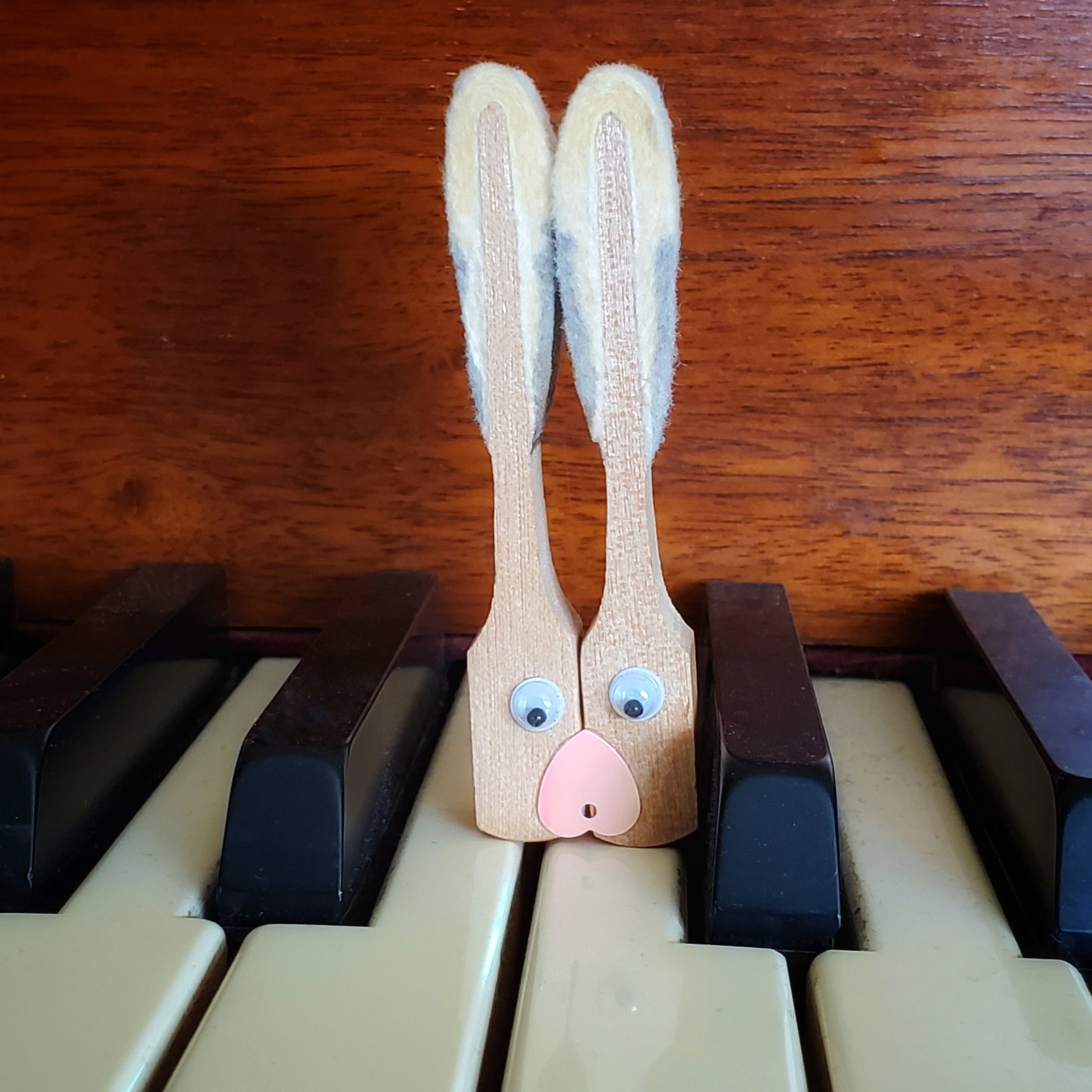 magnet in the shape of a bunny's head - made from 2 upcycled piano hammers - magnet is sitting on a piano keyboad