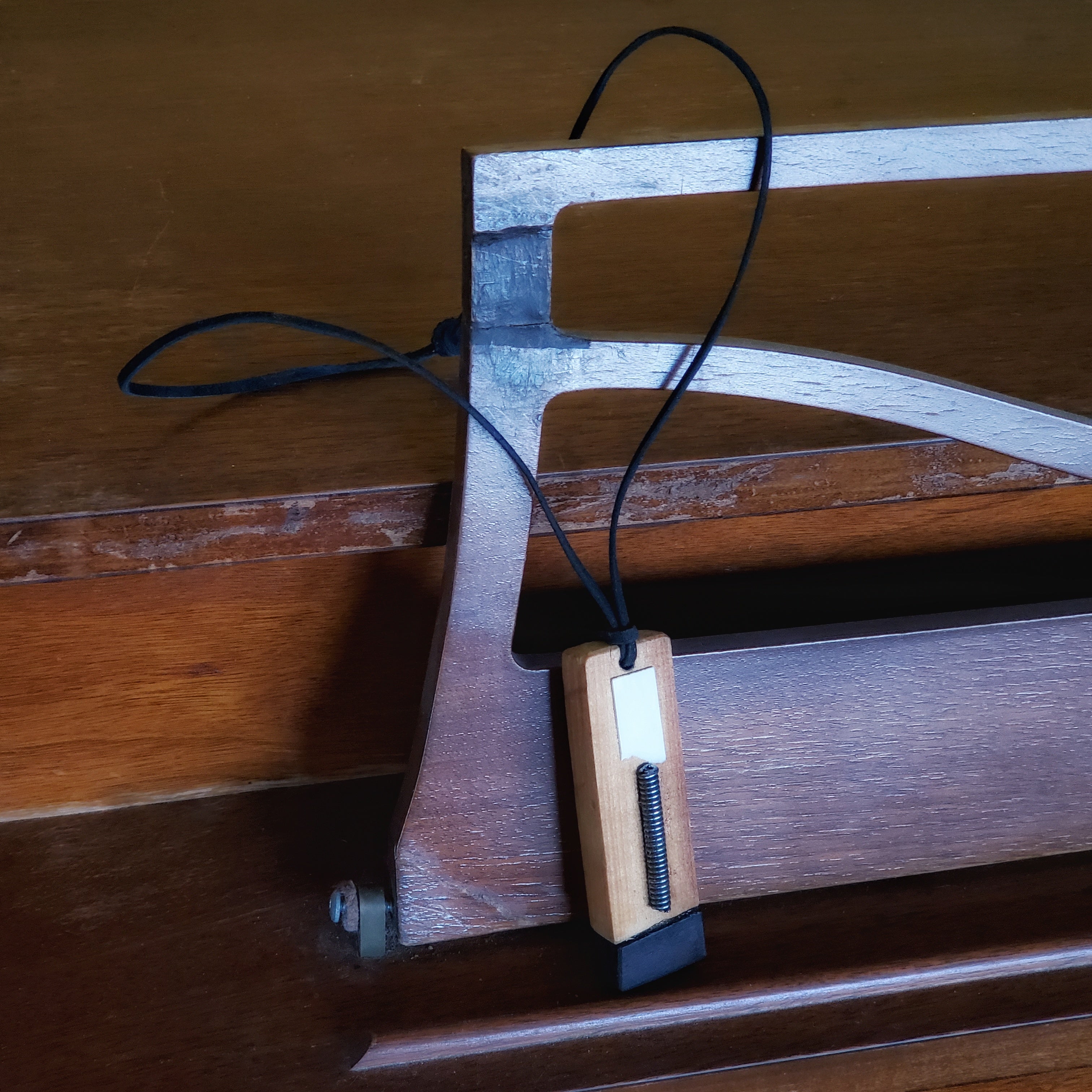 a necklace the pendant of which is made from upcycled pieces of wood, string, ebony and ivory from a piano as well as a leather cord - the necklace hangs on the sheet music holder of a piano