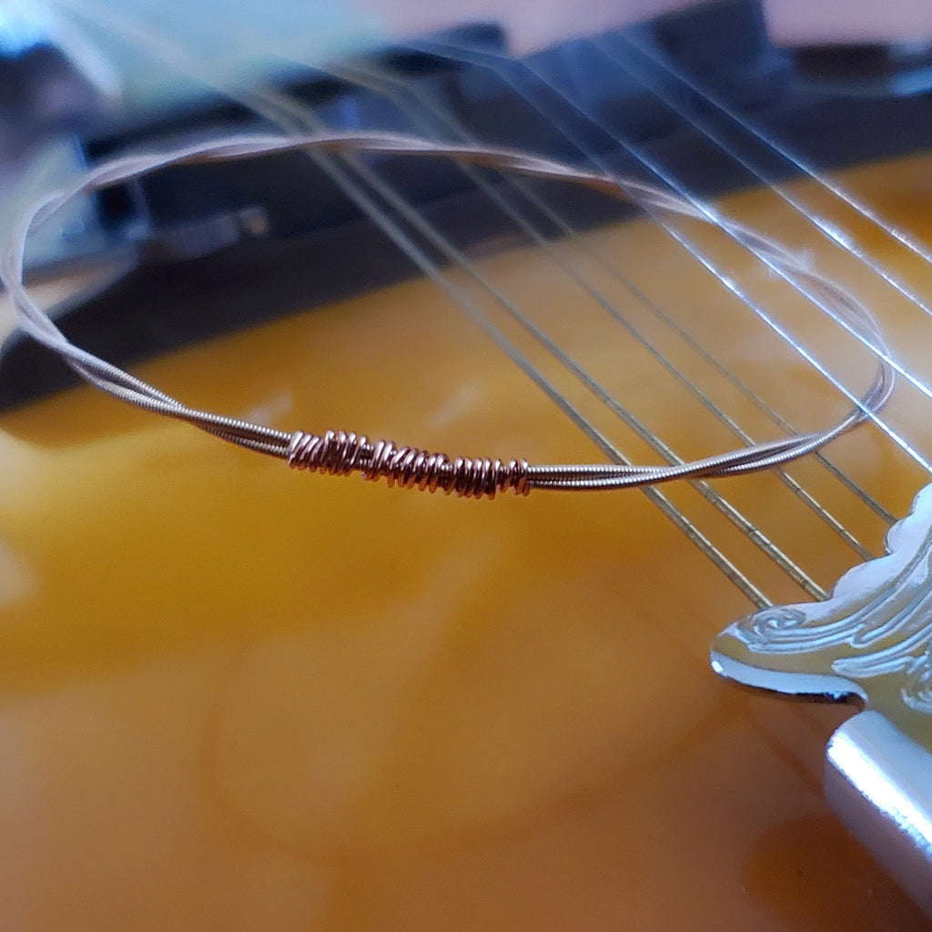 bangle style bracelet made from an upcycled mandolin string sitting on the strings of a gold coloured mandolin