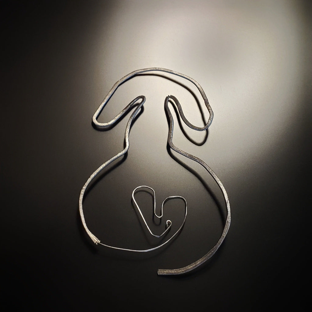 a bookmark in the shape of a dog, made from an upcycled guitar string hammered flat - black and grey background