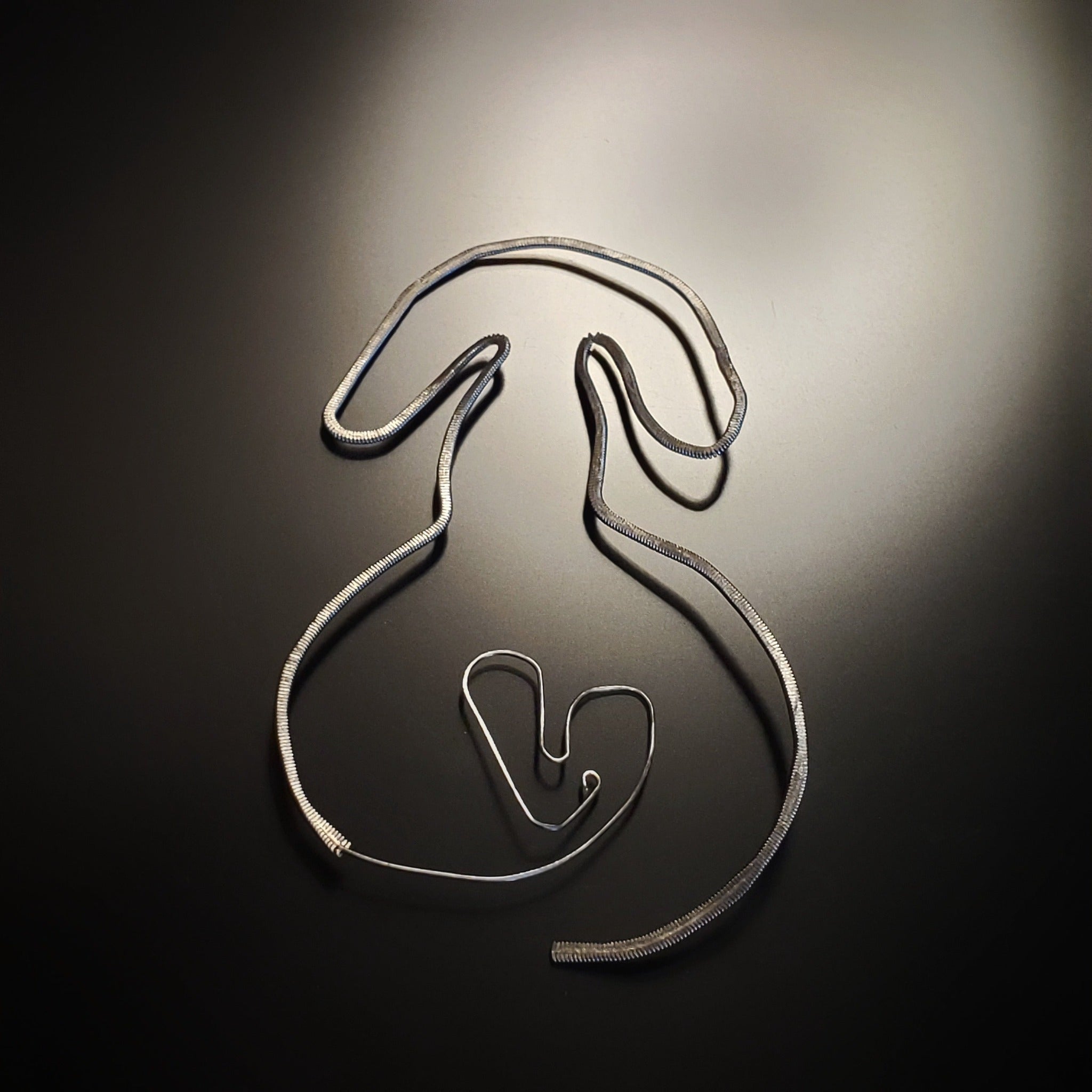 a bookmark in the shape of a dog, made from an upcycled guitar string hammered flat - black and grey background