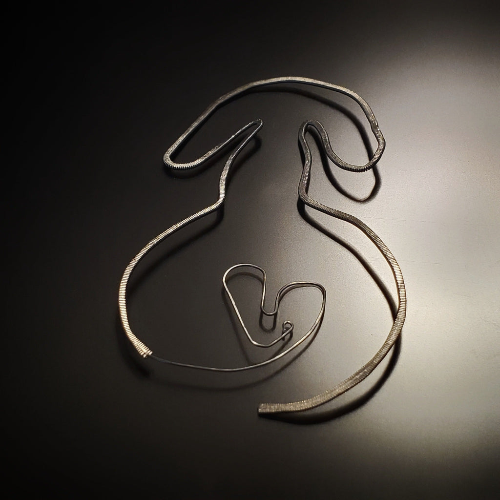 a bookmark in the shape of a dog, made from an upcycled guitar string hammered flat - black and grey background