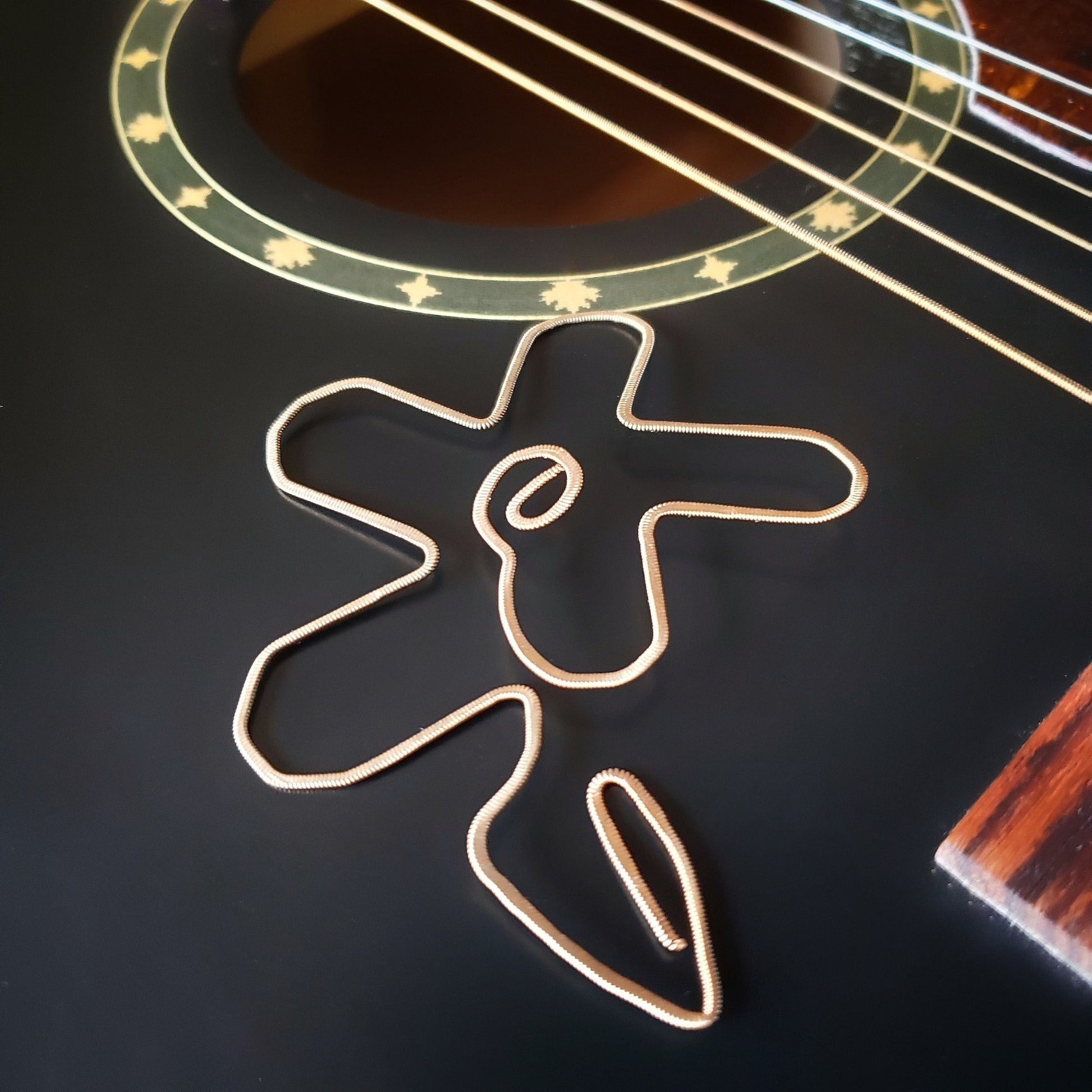 bookmark shaped like a flower made from a hammered guitar string lying the sound hole of  a black guitar