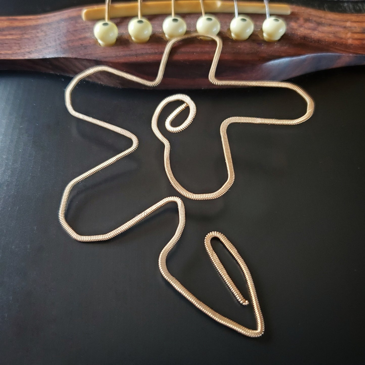 bookmark shaped like a flower made from a hammered guitar string lying partway on the bridge of a black guitar