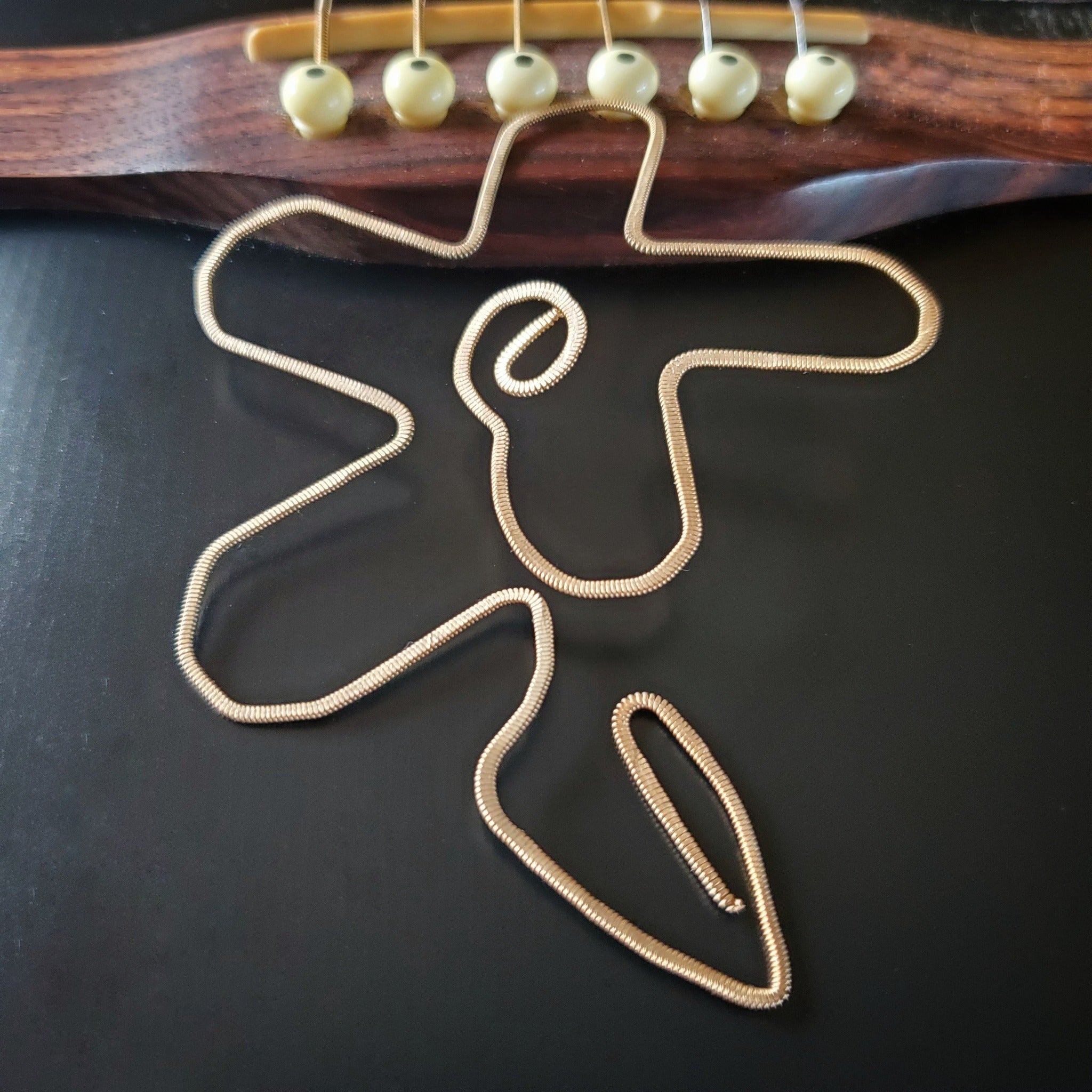 bookmark shaped like a flower made from a hammered guitar string lying partway on the bridge of a black guitar