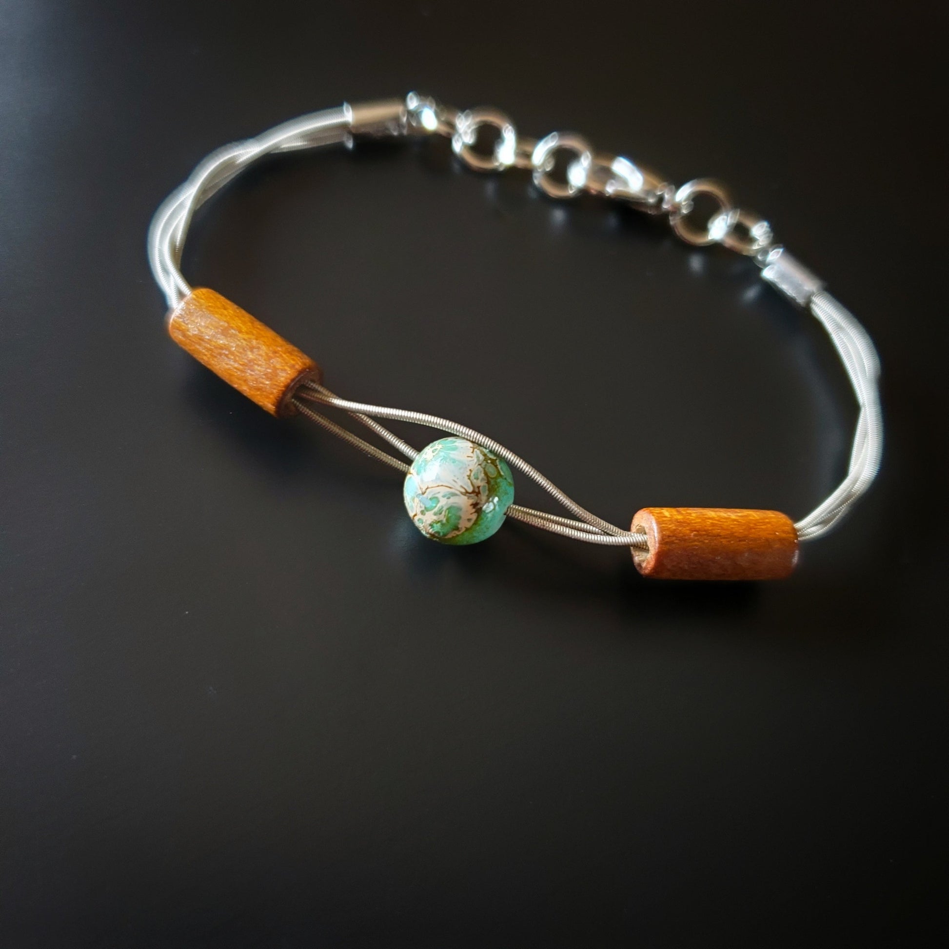 clasp style bracelet made from an upcycled guitar string on which there are two wood bead on either side of a green and gray round bead 