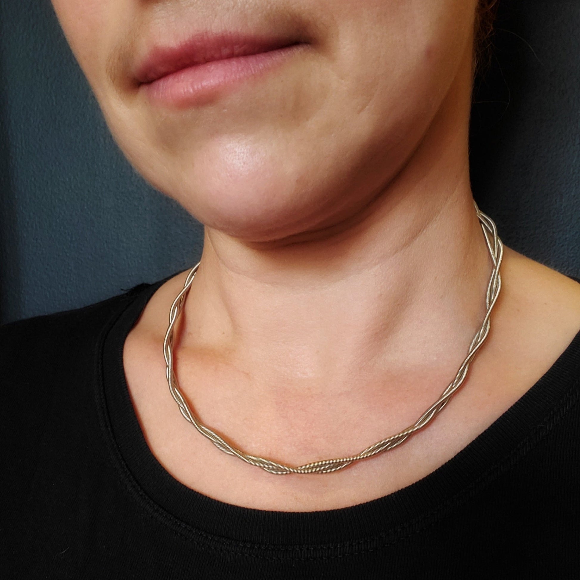 picture of a woman's neck wearing a silver coloured bass guitar string necklace (two string twisted).
