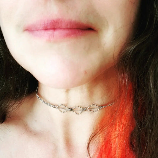 part of a woman's face and neck - brown and orange curly hair - on her neck is a necklace in the shape of 3 diamonds made from upcycled guitar strings