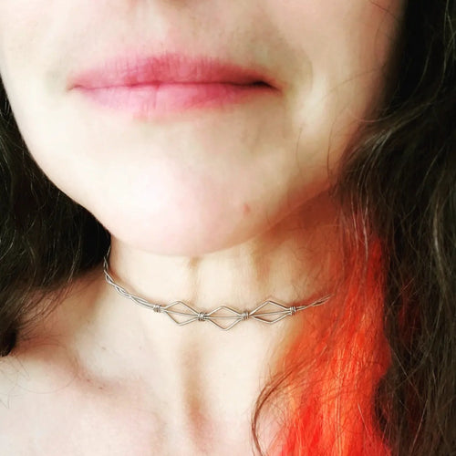 partie du visage et du cou d'une femme - cheveux bouclés bruns et oranges - autour de son cou se trouve un collier en forme de 3 diamants fabriqué à partir de cordes de guitare recyclées