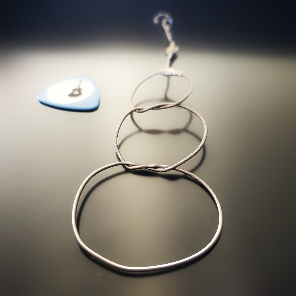 Christmas ornament in the shape of a snowman, made from an upcycled guitar string - on the left is a blue guitar pick with an image of a black guitar