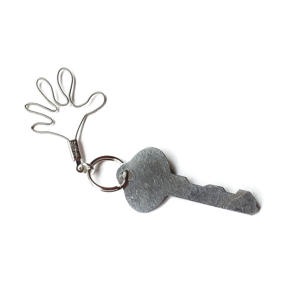 a keychain made from an upcycled guitar string shaped like a hand attached to a silver key- white background
