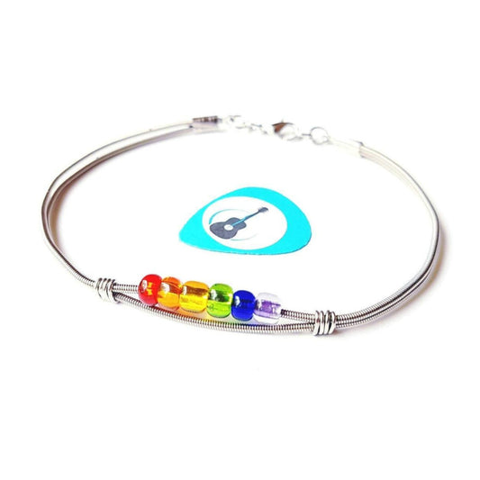 clasp style bracelet made from an upcycled guitar string - 6 glass beads represent the colours of the LGBTQ flag (red, orange, yellow, green, blue and purple) - blue guitar pick with an image of a black guitar - white background