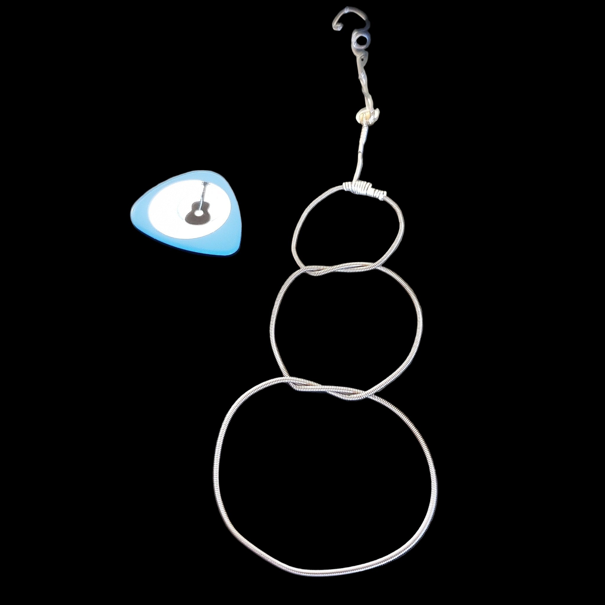Christmas ornament in the shape of a snowman, made from an upcycled guitar string - on the left is a blue guitar pick with an image of a black guitar