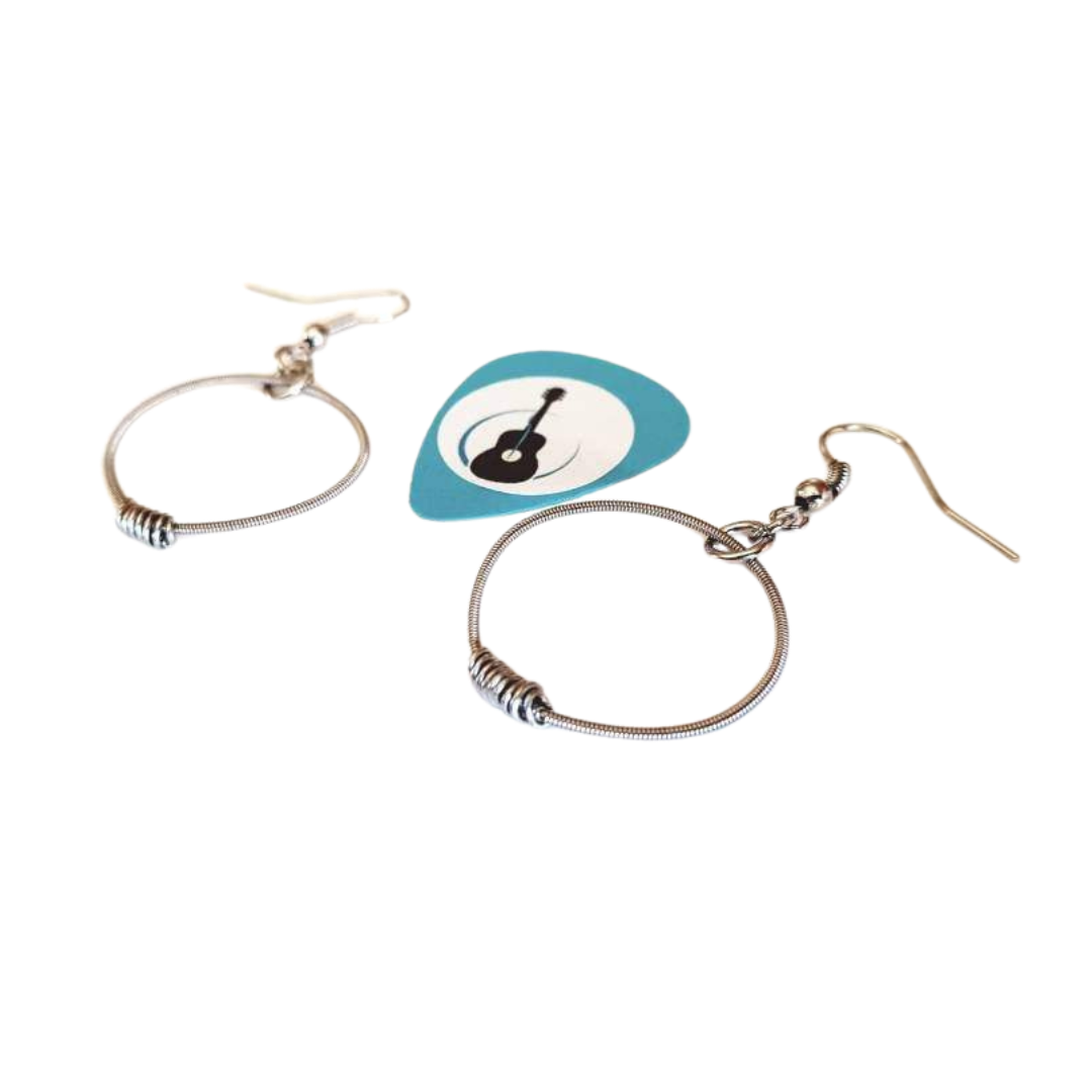 small hoop style earrings made from upcycled guitar strings in between the two is a blue guitar pick with an image of a black guitar white background