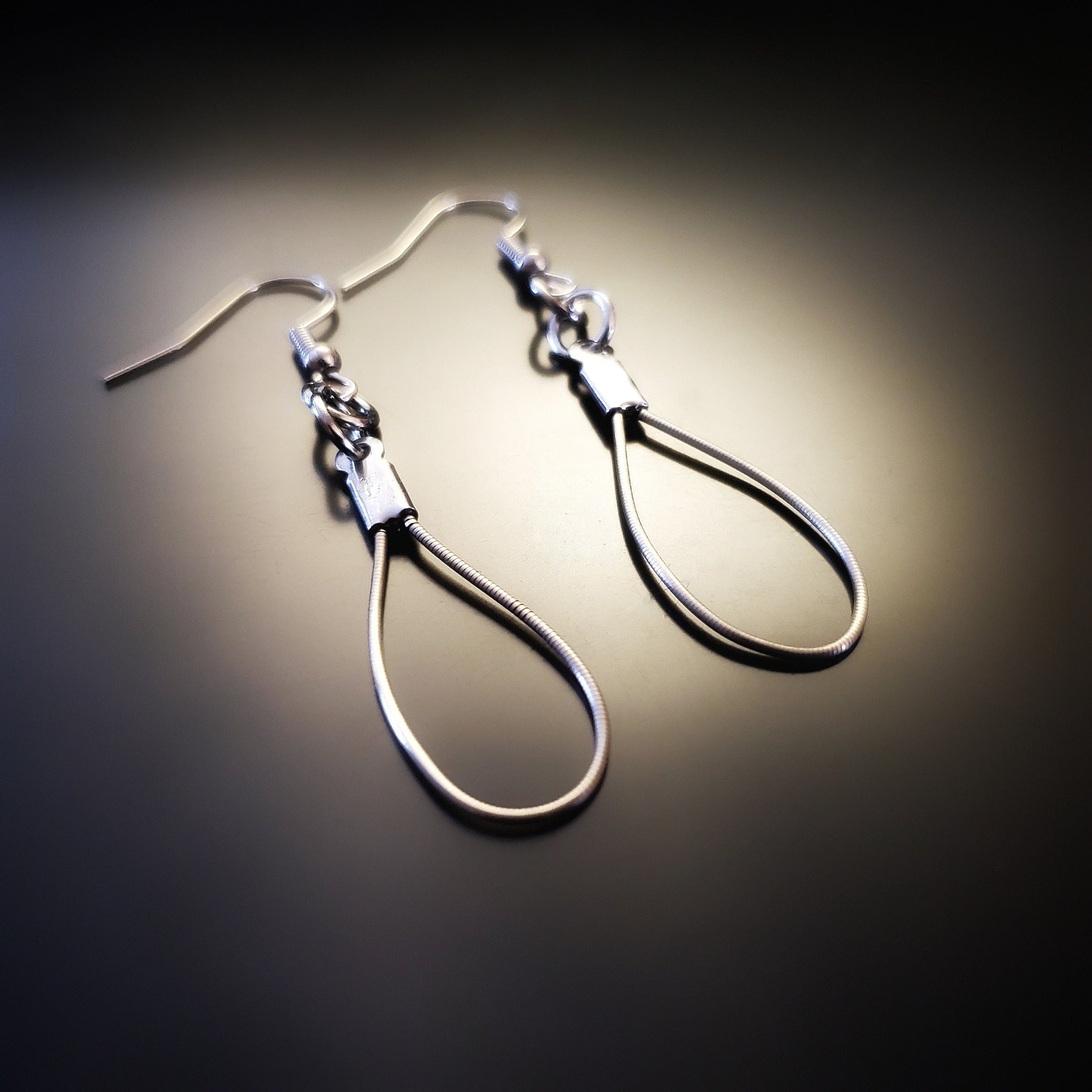 a pair of teardrop style earrings made from upcycled violin strings on black background