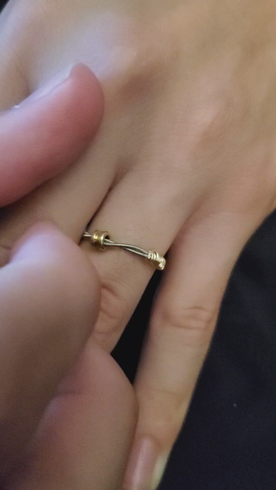 video of a hand wearing a guitar string fidget ring with a gold coloured ballend the fingers of a second hand is flicking the ballend to make it move