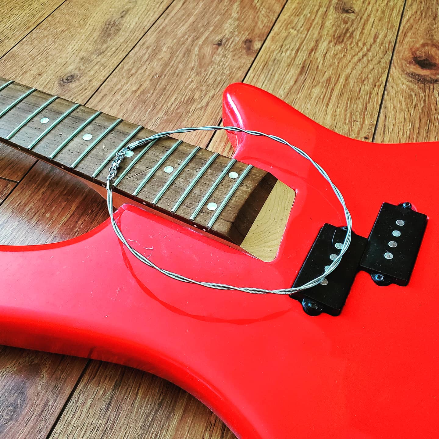 silver coloured bass guitar string necklace lying on a red bass guitar which does not have any strings