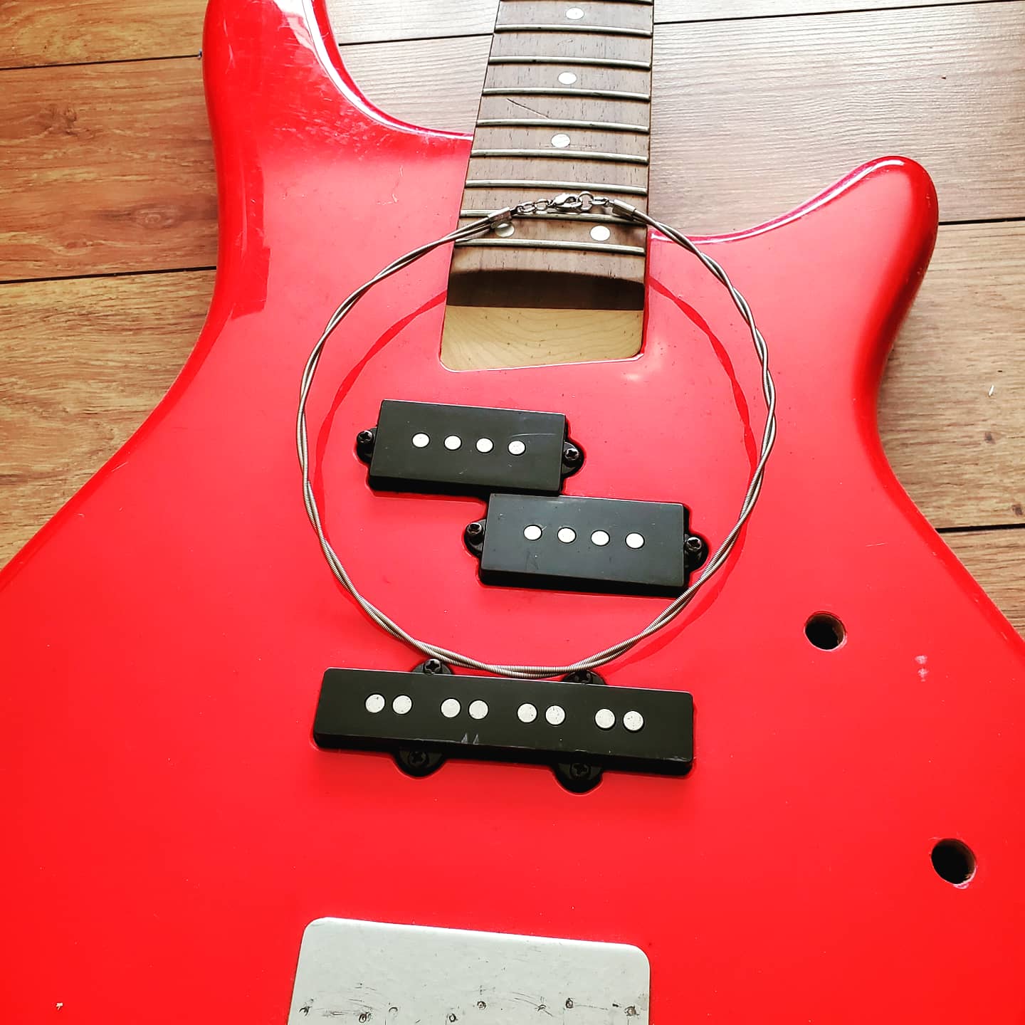 a silver coloured bass guitar string necklace (two string twisted) lying on top of a red bass guitar that has the strings removed with a wood background